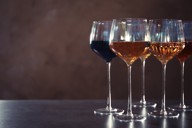 Elegant glasses with different wines on table against brown background