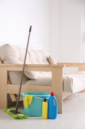 Photo of Floor mop, cleaning detergents and bucket with gloves in living room