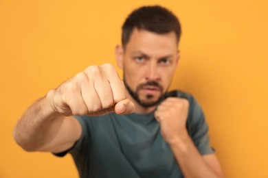Photo of Man throwing punch against orange background, focus on fist. Space for text