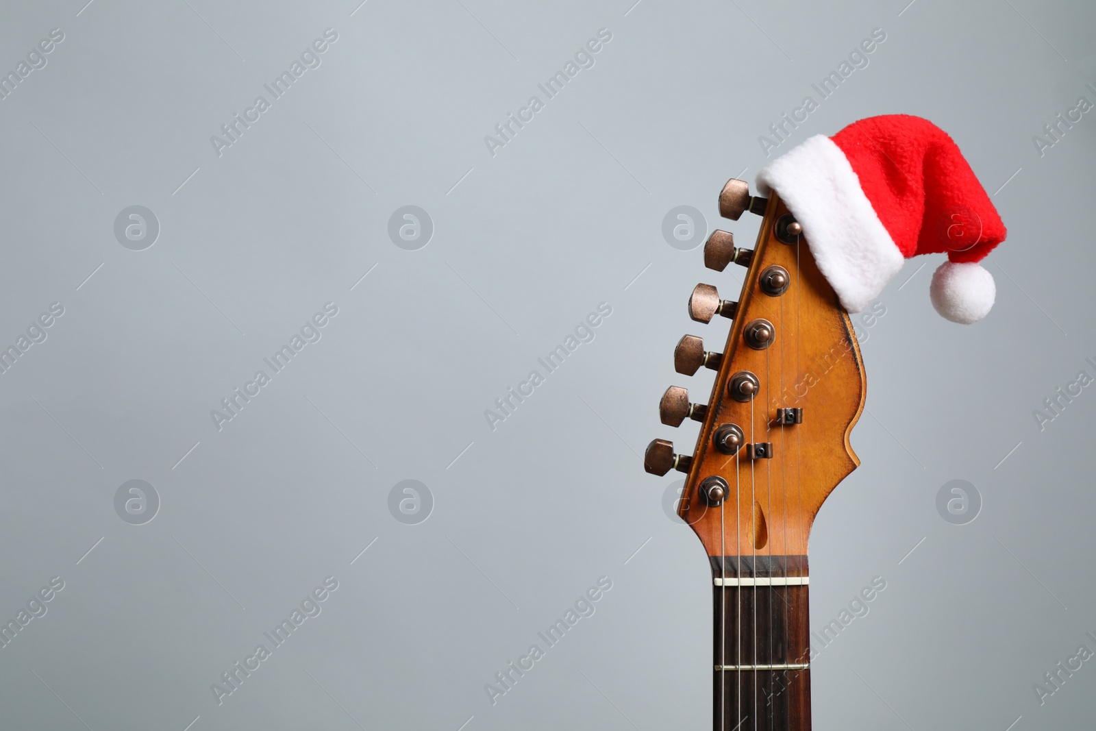 Photo of Guitar with Santa hat on grey background, space for text. Christmas music