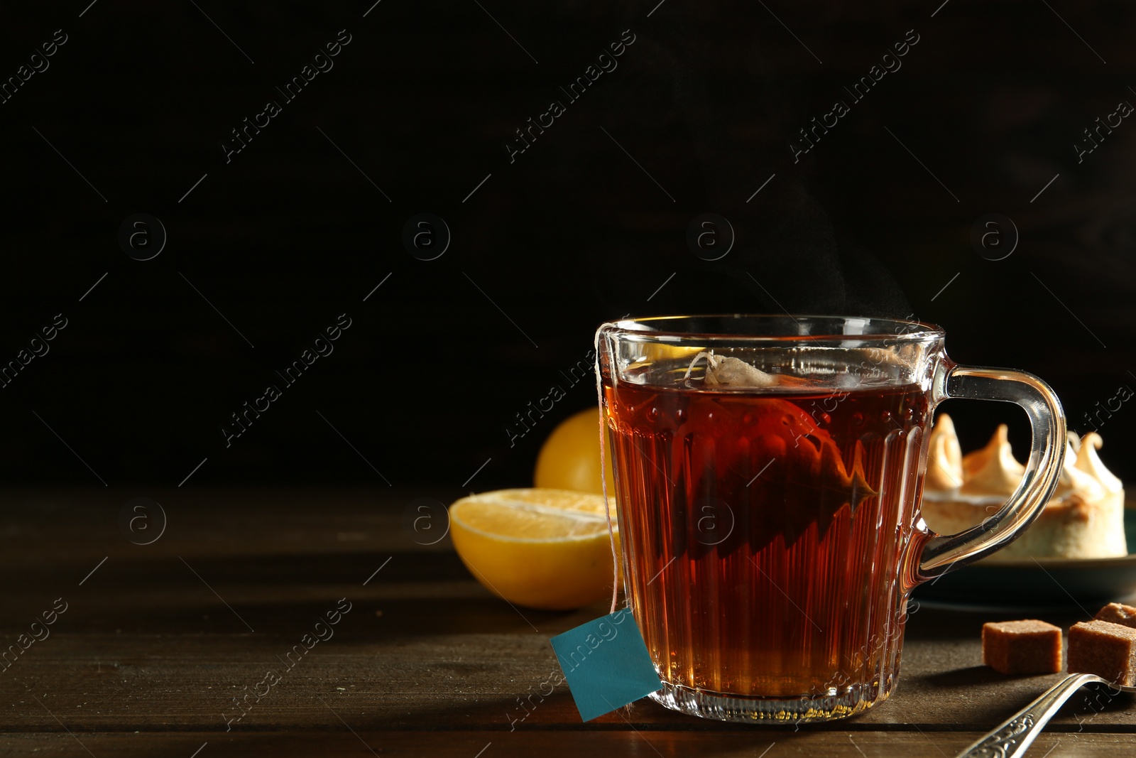 Photo of Tea bag in glass cup of hot water on dark wooden table. Space for text