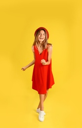 Beautiful young woman in red dress dancing on yellow background