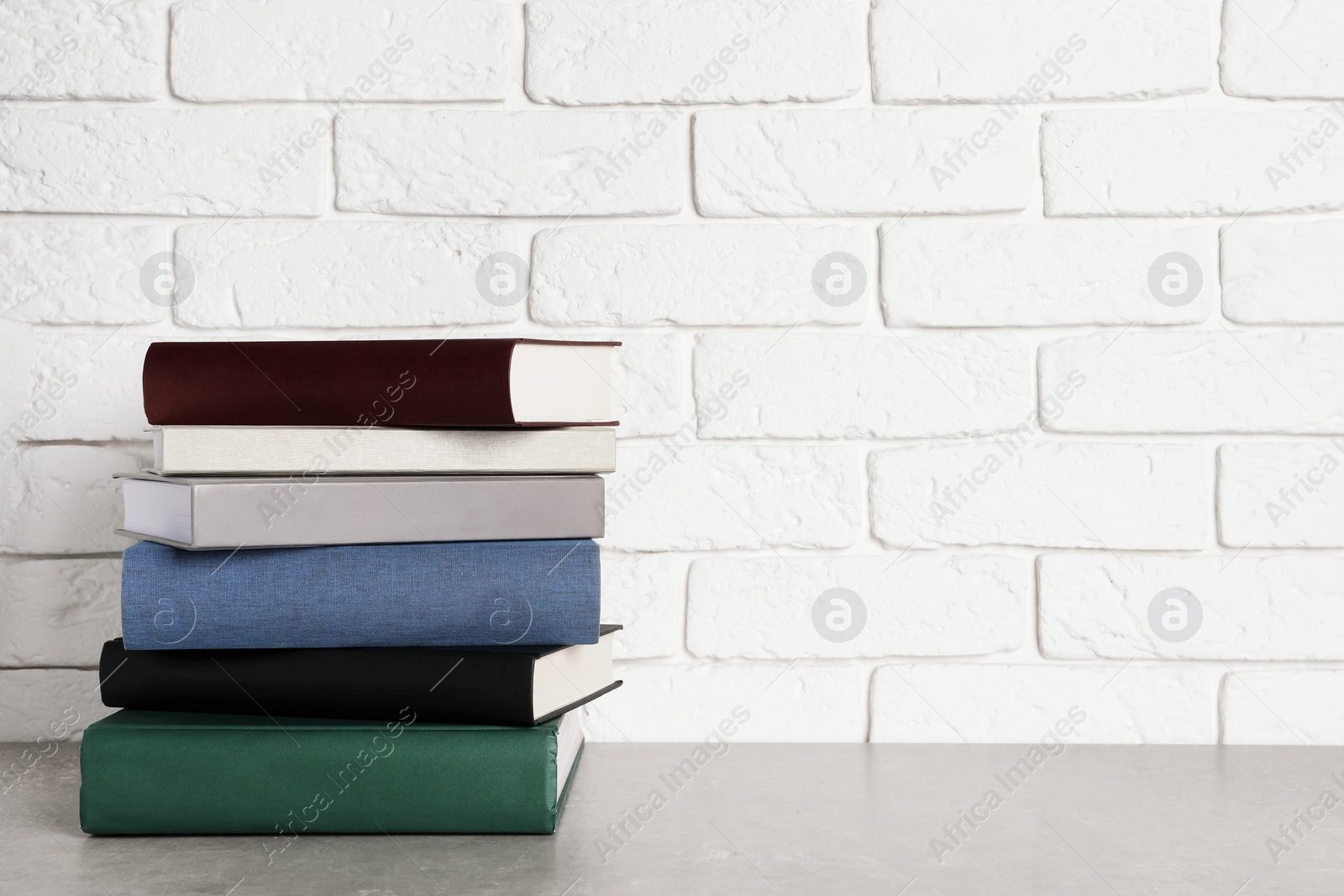 Photo of Stack of hardcover books on grey table near white brick wall, space for text