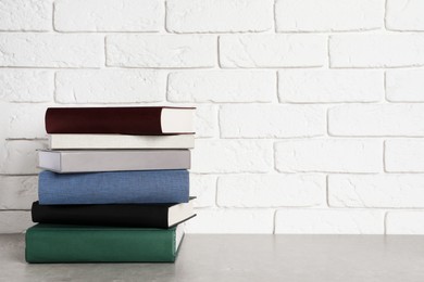 Photo of Stack of hardcover books on grey table near white brick wall, space for text