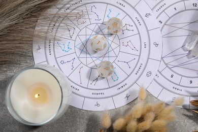 Zodiac wheel, natal chart, burning candle and astrology dices on grey table, flat lay