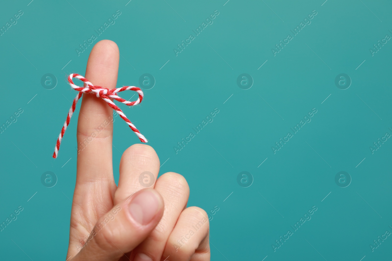 Photo of Woman showing index finger with tied bow as reminder on light blue background, closeup. Space for text