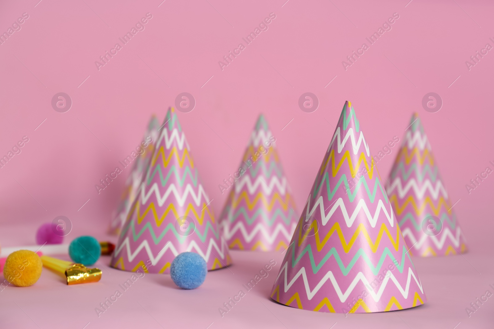 Photo of Colorful party hats, blower and fluffy balls on pink background