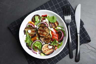 Photo of Delicious salad with roasted eggplant, cheese and arugula served on black table, flat lay