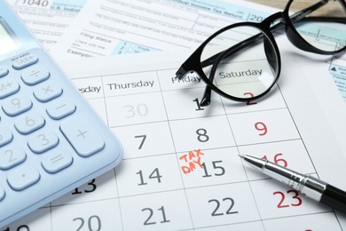 Tax day. Calendar with date reminder, documents, pen, glasses and calculator on table