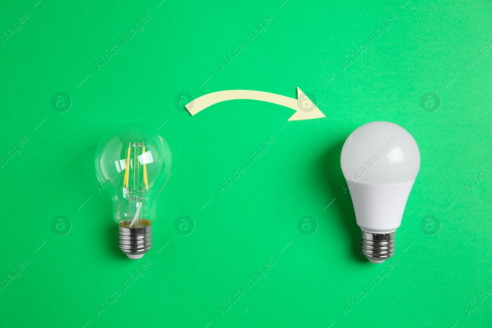 Photo of LED and simple light bulbs with arrow on green background, flat lay. Energy saving concept