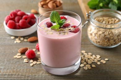 Photo of Glass of tasty raspberry smoothie with oatmeal and mint on wooden table