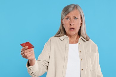 Photo of Worried woman with credit card on light blue background. Be careful - fraud