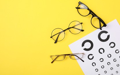 Photo of Vision test chart and glasses on yellow background, flat lay. Space for text