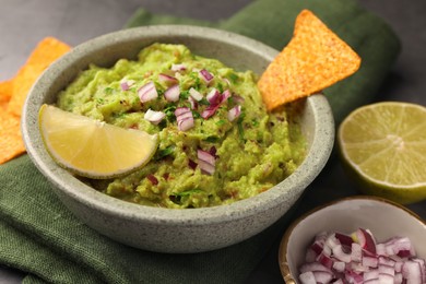 Photo of Bowl of delicious guacamole, nachos chips and lime on table, closeup