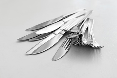 Photo of Knives and forks on white table, closeup