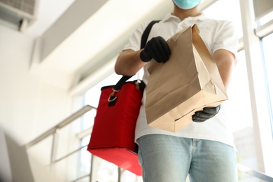 Photo of Courier in protective mask and gloves with order indoors, closeup. Restaurant delivery service during coronavirus quarantine