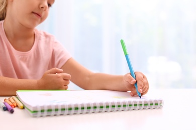 Photo of Little left-handed girl drawing at table in room, closeup