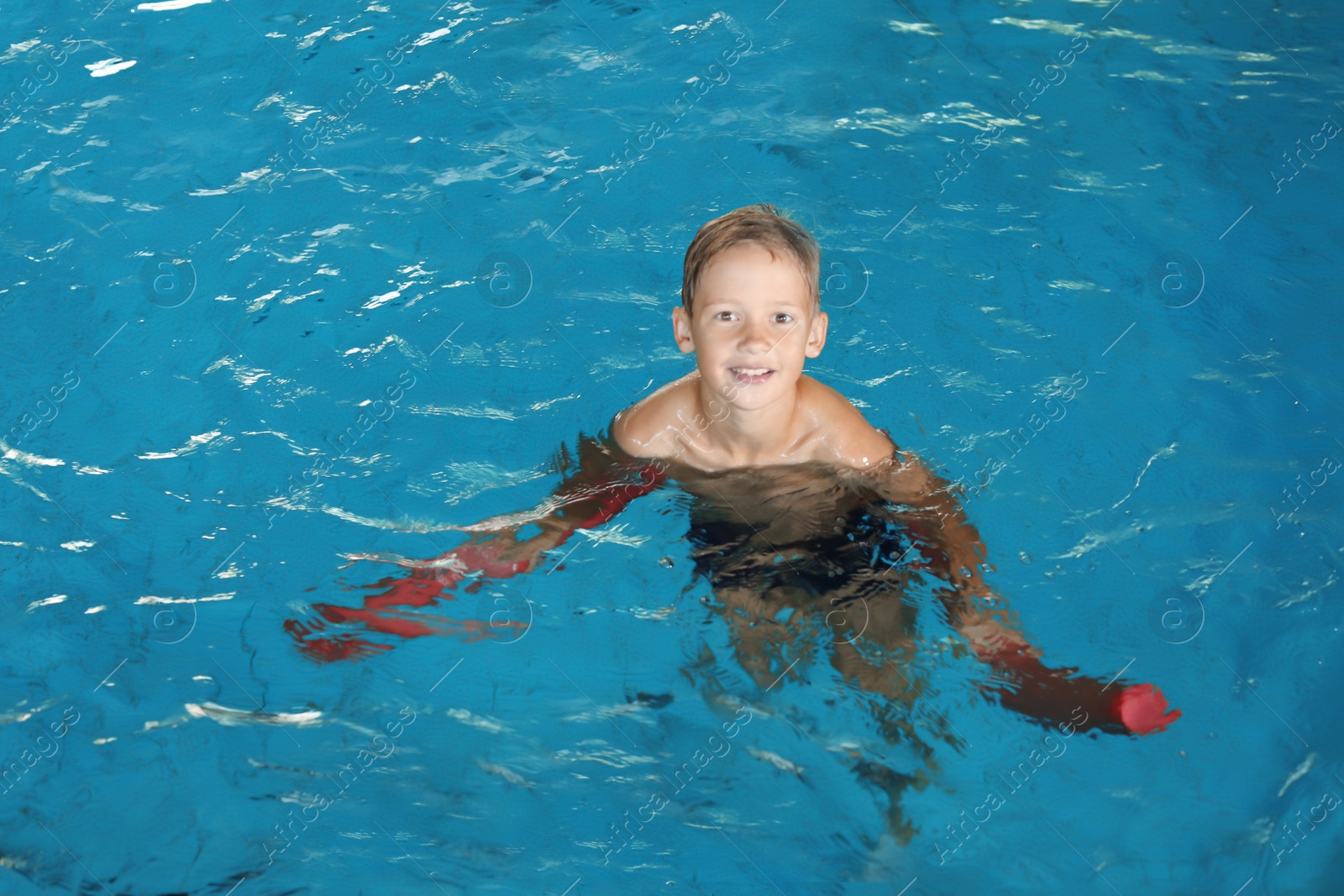 Photo of Little boy with swimming noodle in indoor pool