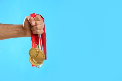 Man holding golden medals on light blue background, closeup. Space for design
