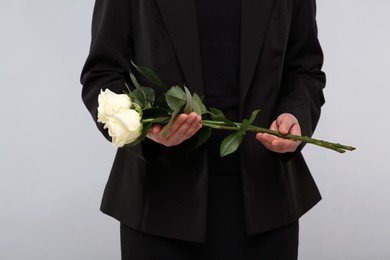 Woman with white rose flowers on light grey background, closeup. Funeral ceremony