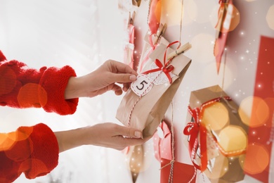 Image of Woman hanging paper bag with gift on white wall, closeup. Christmas advent calendar