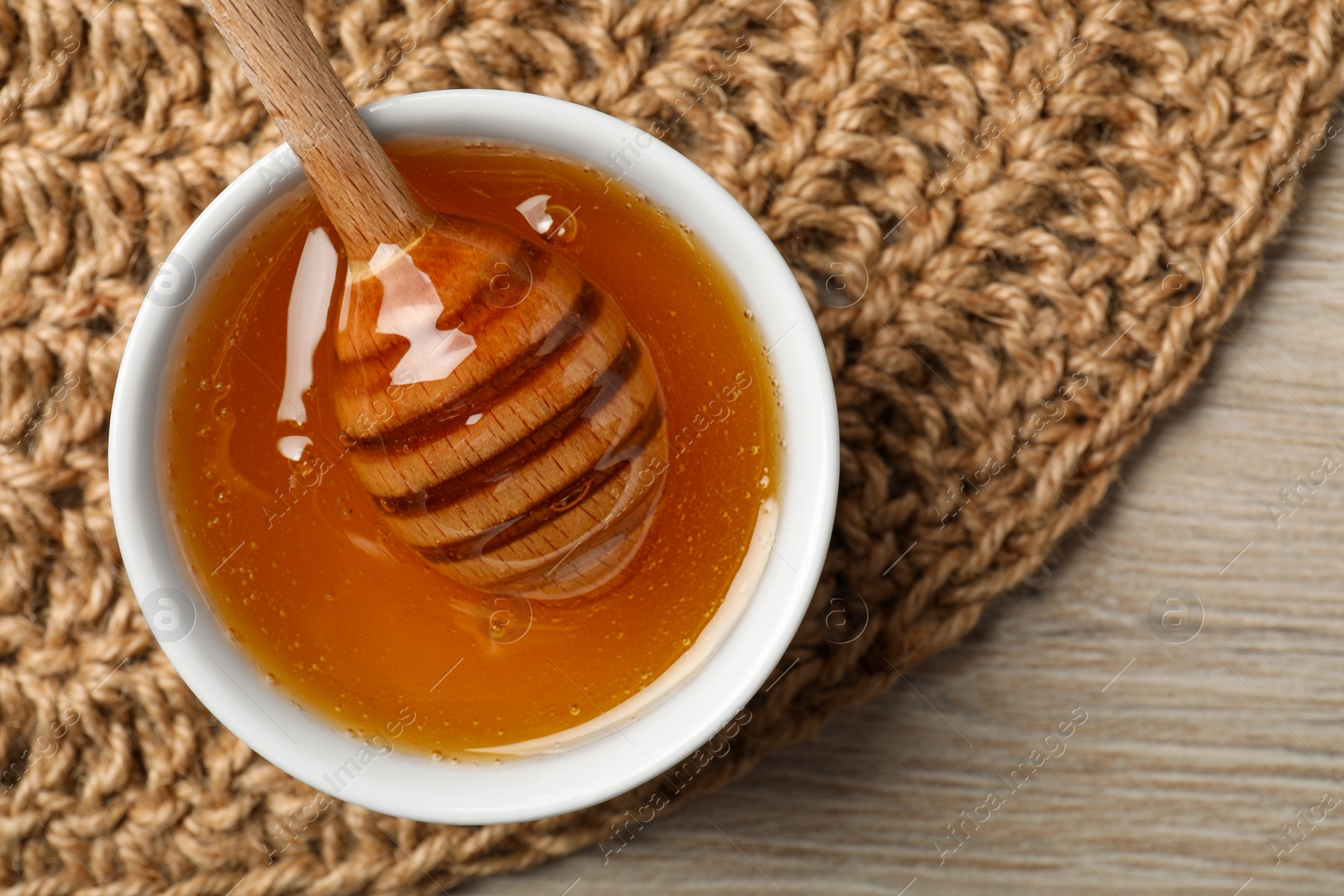 Photo of Dipper with honey in bowl on wooden table, top view. Space for text