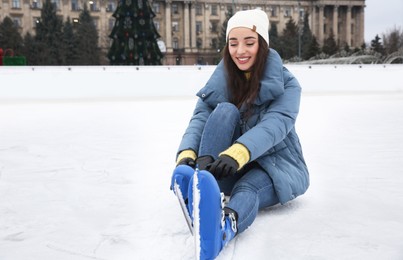Image of Woman adjusting figure skate while sitting on ice rink. Space for text