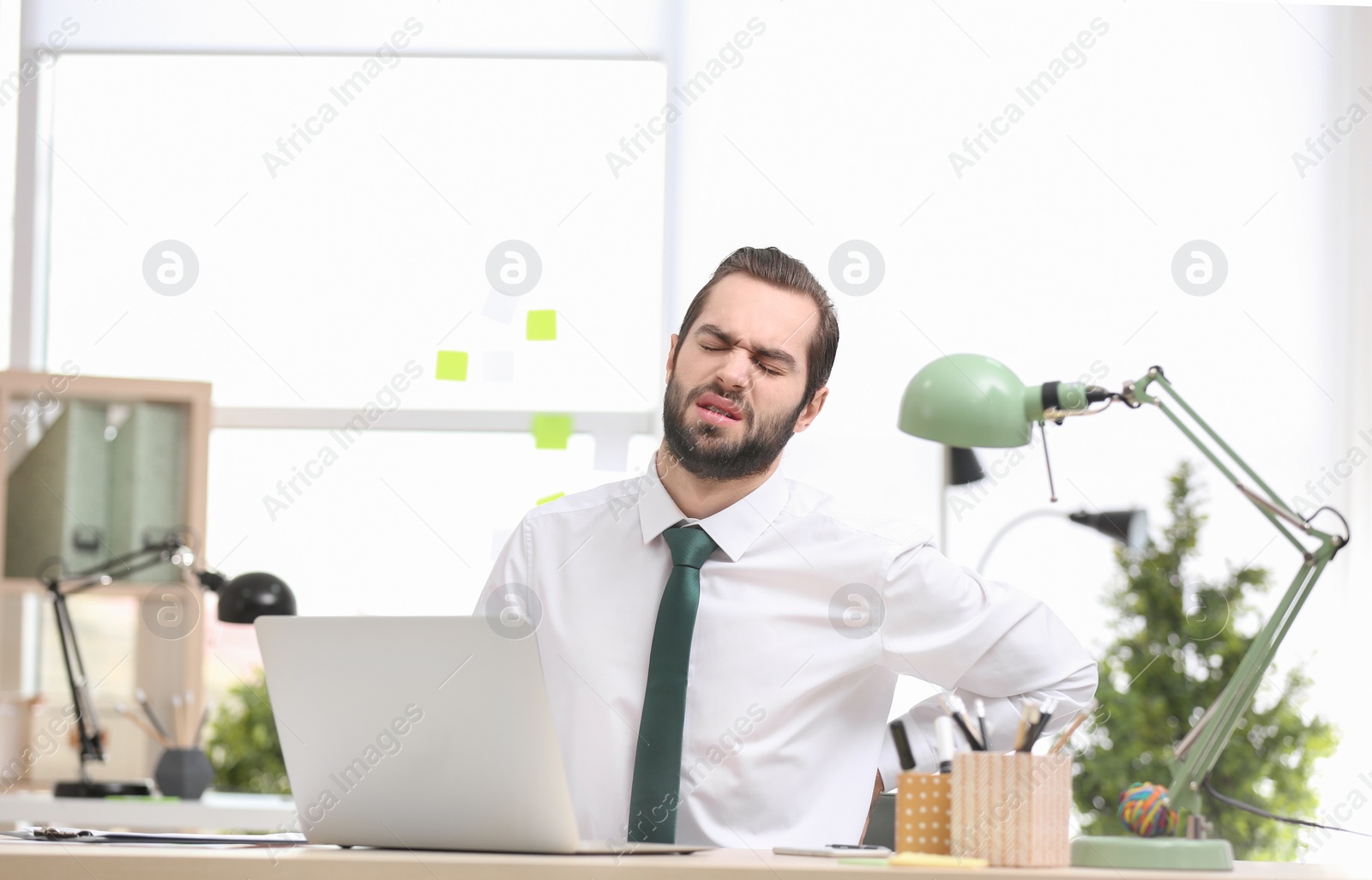 Photo of Young man suffering from back pain in office