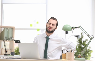 Photo of Young man suffering from back pain in office