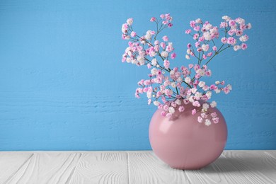 Photo of Beautiful dyed gypsophila flowers in pink vase on white wooden table against light blue background. Space for text