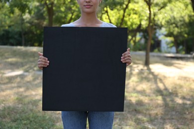Photo of Woman holding blank poster outdoors, closeup. Mockup for design	