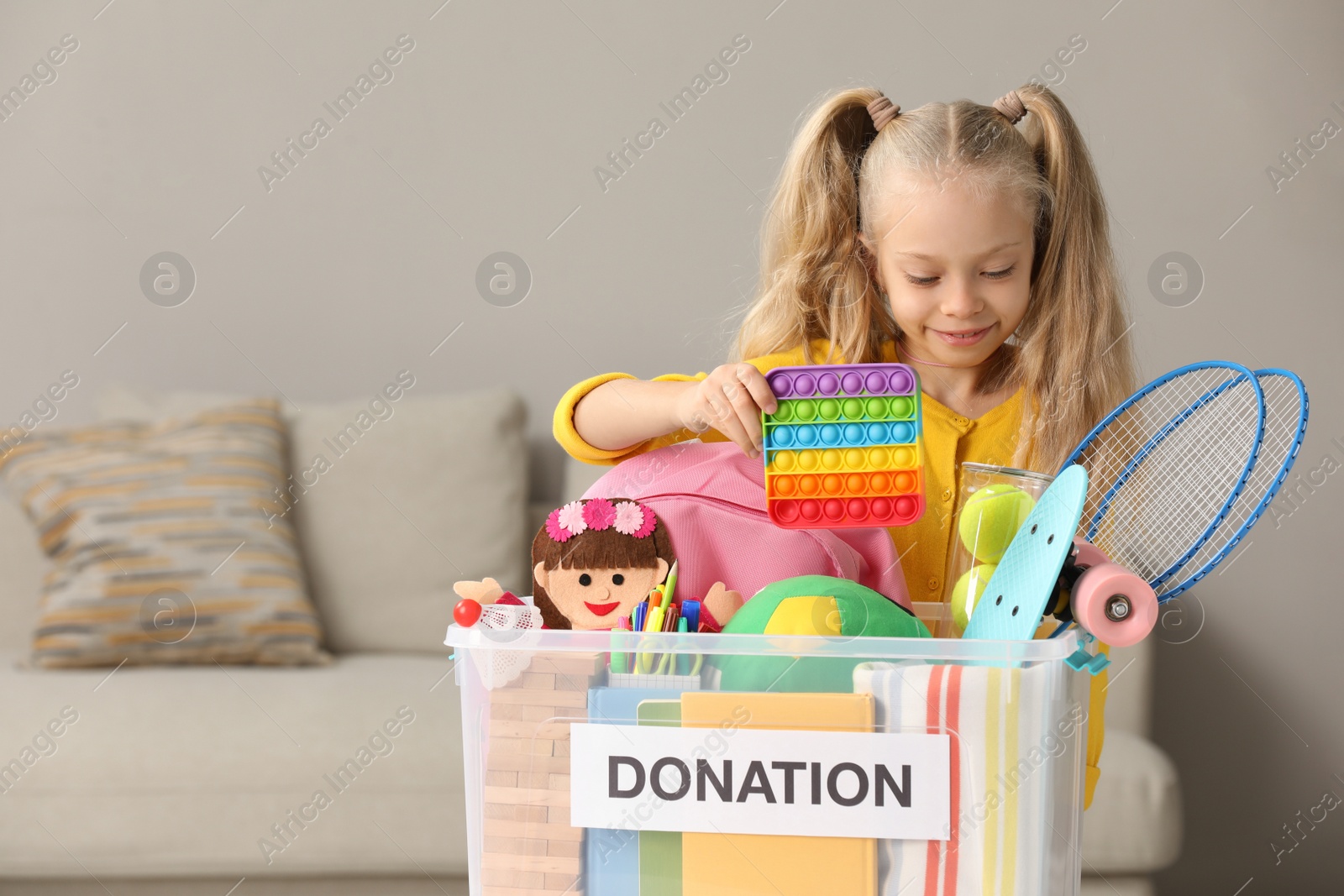 Photo of Cute little girl putting toy into donation box at home, space for text