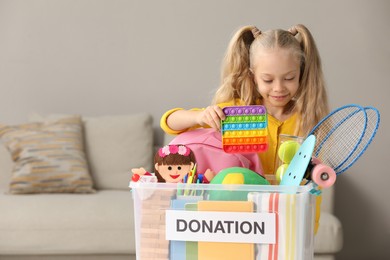 Photo of Cute little girl putting toy into donation box at home, space for text