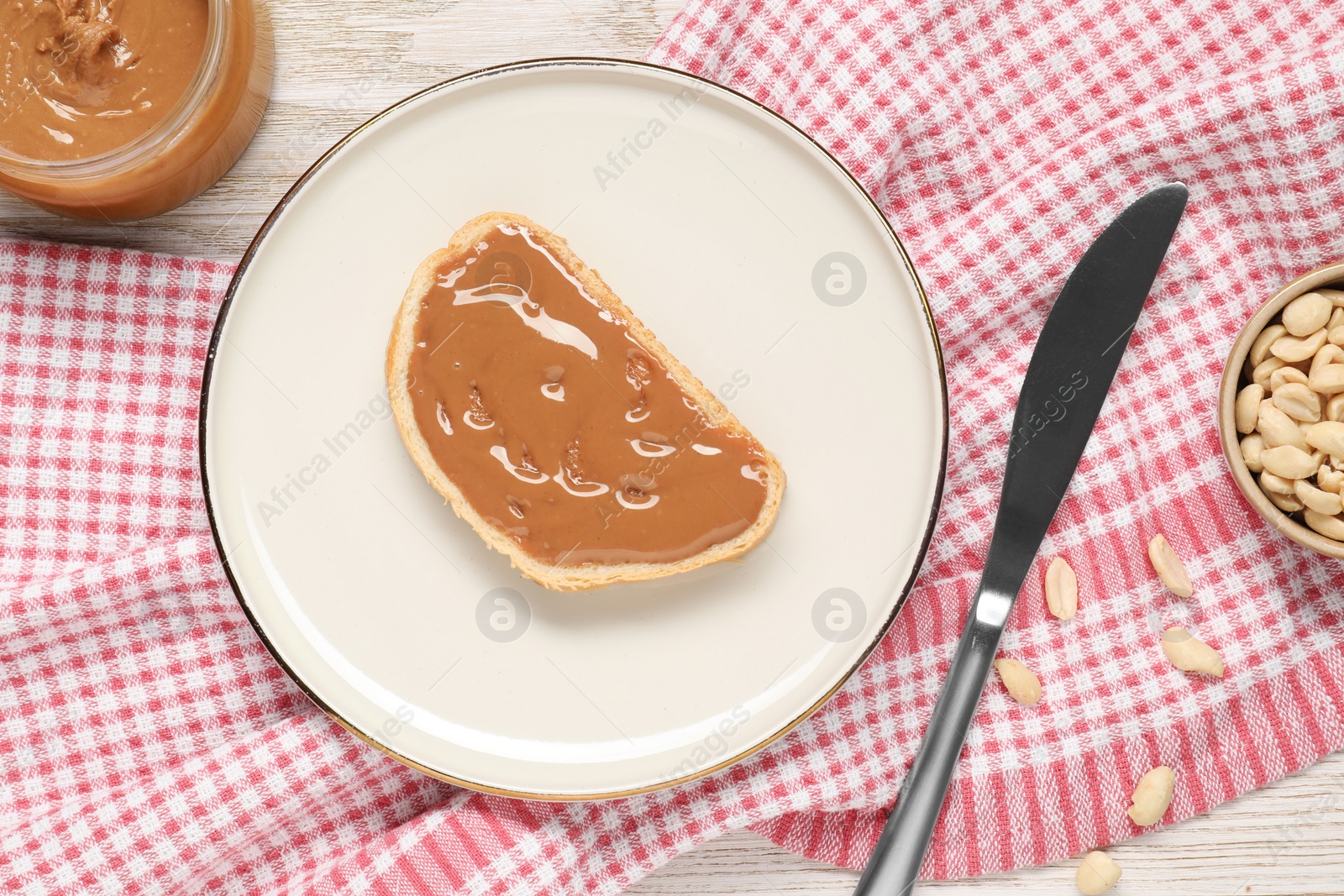 Photo of Toast with tasty nut butter, knife and peanuts on white table, flat lay