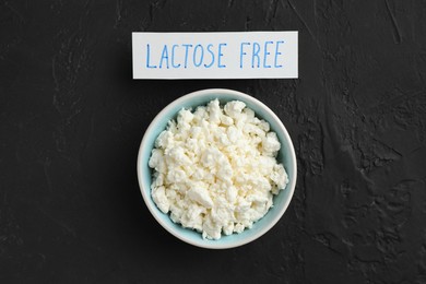 Photo of Cottage cheese and card with phrase Lactose free on black textured table, top view