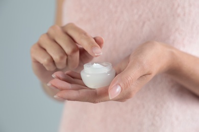 Young woman holding jar of cream on grey background, closeup