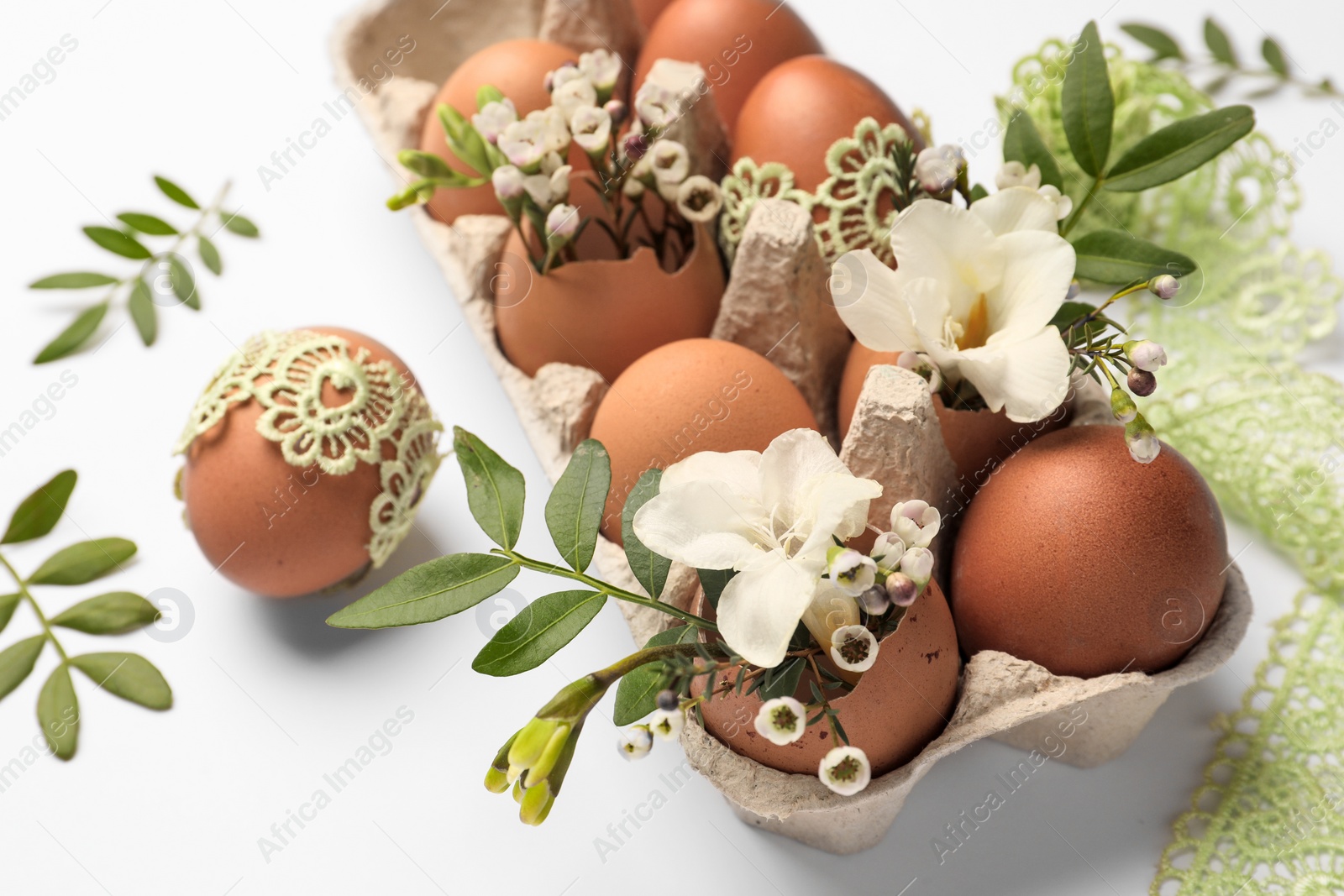 Photo of Easter eggs, twigs, flowers and lace ribbon on white background, closeup