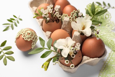 Photo of Easter eggs, twigs, flowers and lace ribbon on white background, closeup