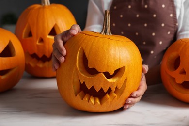 Photo of Woman with carved pumpkins for Halloween at white marble table, closeup