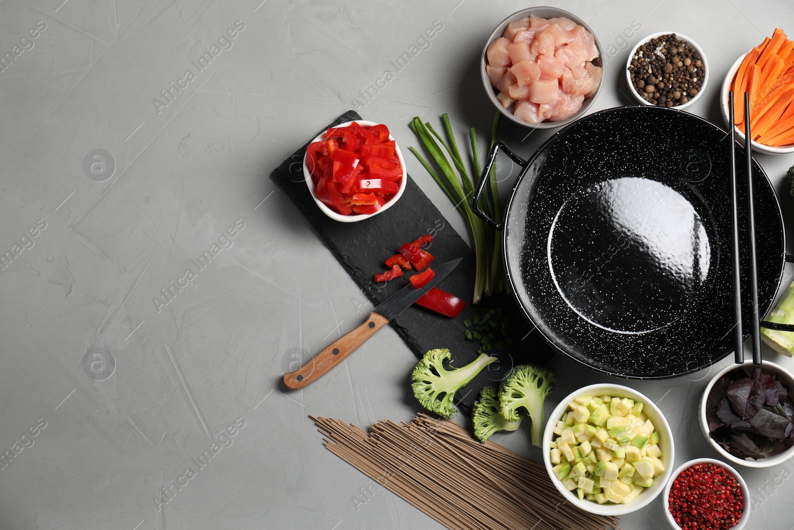 Photo of Wok pan, noodles, chicken and other products on light grey table, flat lay. Space for text