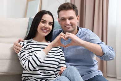 Photo of Happy couple making heart with hands at home