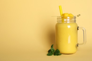 Photo of Mason jar of tasty smoothie with straw, mango and mint leaves on beige background. Space for text