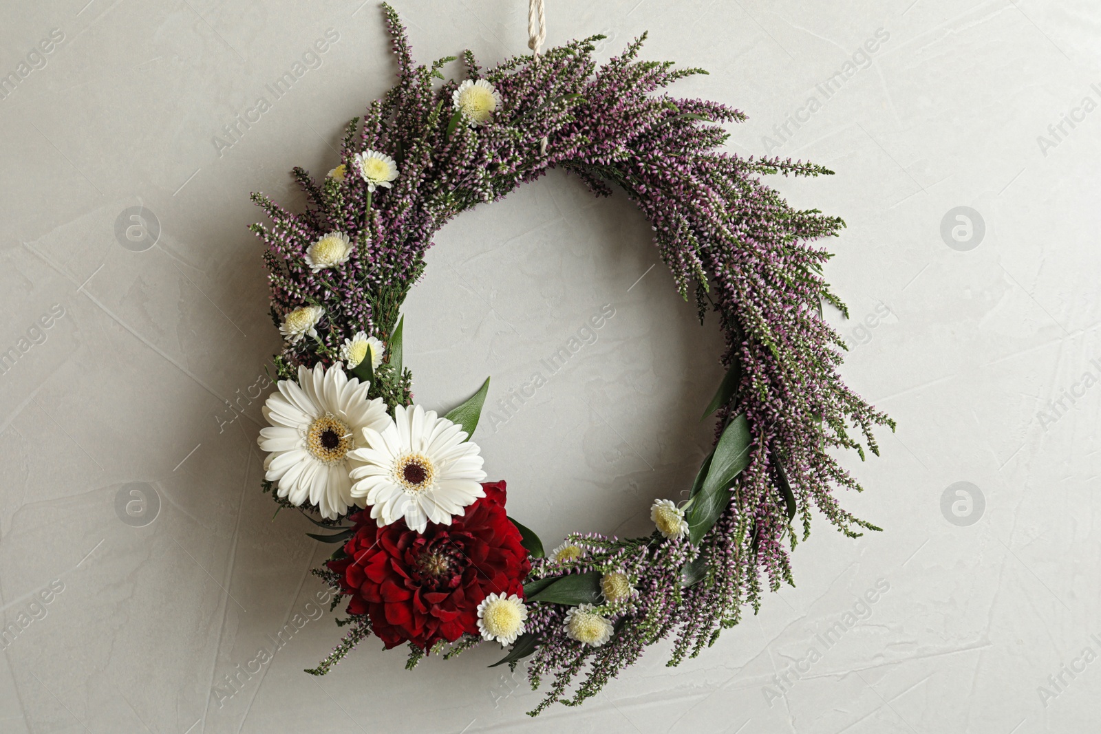 Photo of Beautiful autumnal wreath with heather flowers hanging on light grey background. Space for text