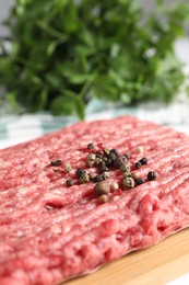 Raw ground meat and peppercorns on table, closeup