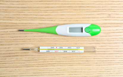 Photo of Modern digital and mercury thermometers on wooden table, flat lay