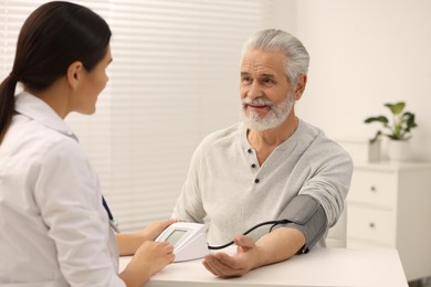 Photo of Nurse measuring elderly patient's blood pressure at white table in hospital