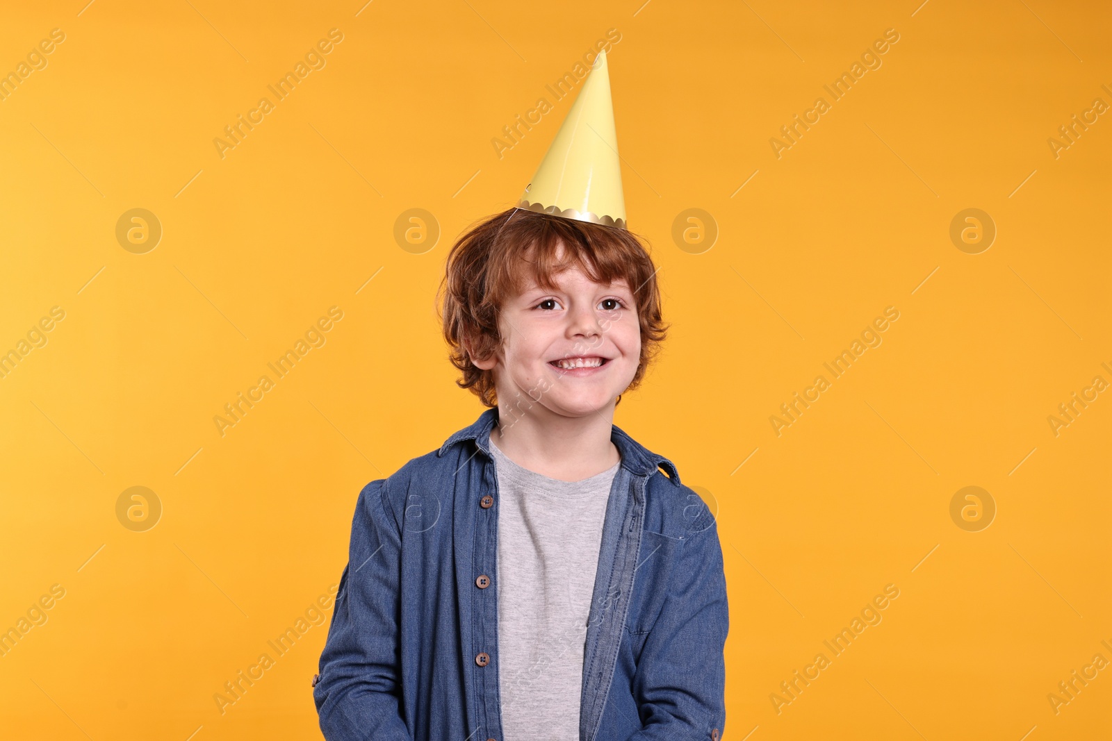 Photo of Birthday celebration. Cute little boy in party hat on orange background