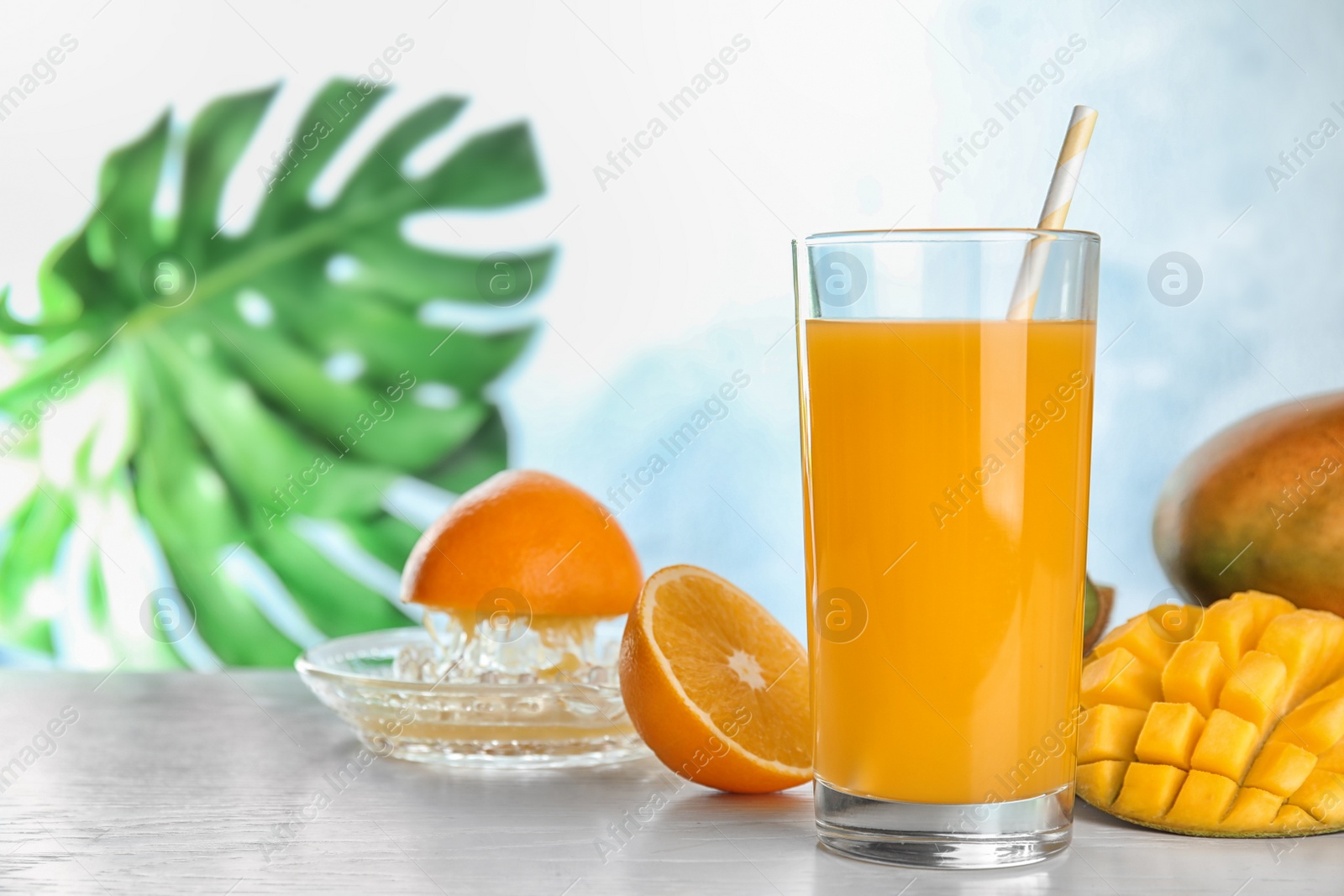 Photo of Glass of fresh mango drink and tropical fruits on table against color background. Space for text