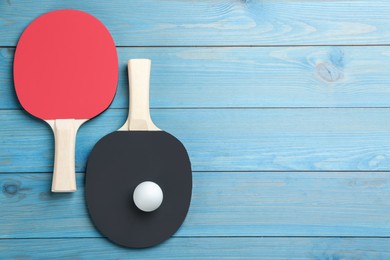 Photo of Ping pong rackets and ball on light blue wooden table, flat lay. Space for text