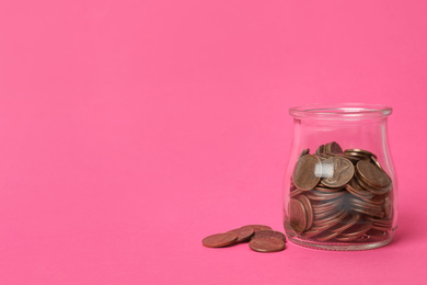 Glass jar with coins on pink background, space for text